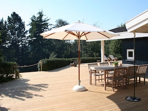 An outdoor deck with a table and chairs, surrounded by a wooden deck and a hedge. - Splendid Holiday Home in Dronningmolle near Beach (Dronningmolle)