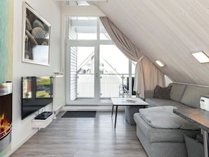 Um quarto moderno no estilo loft, com uma janela grande, televisão de tela plana, lareira e um sofá cinza.