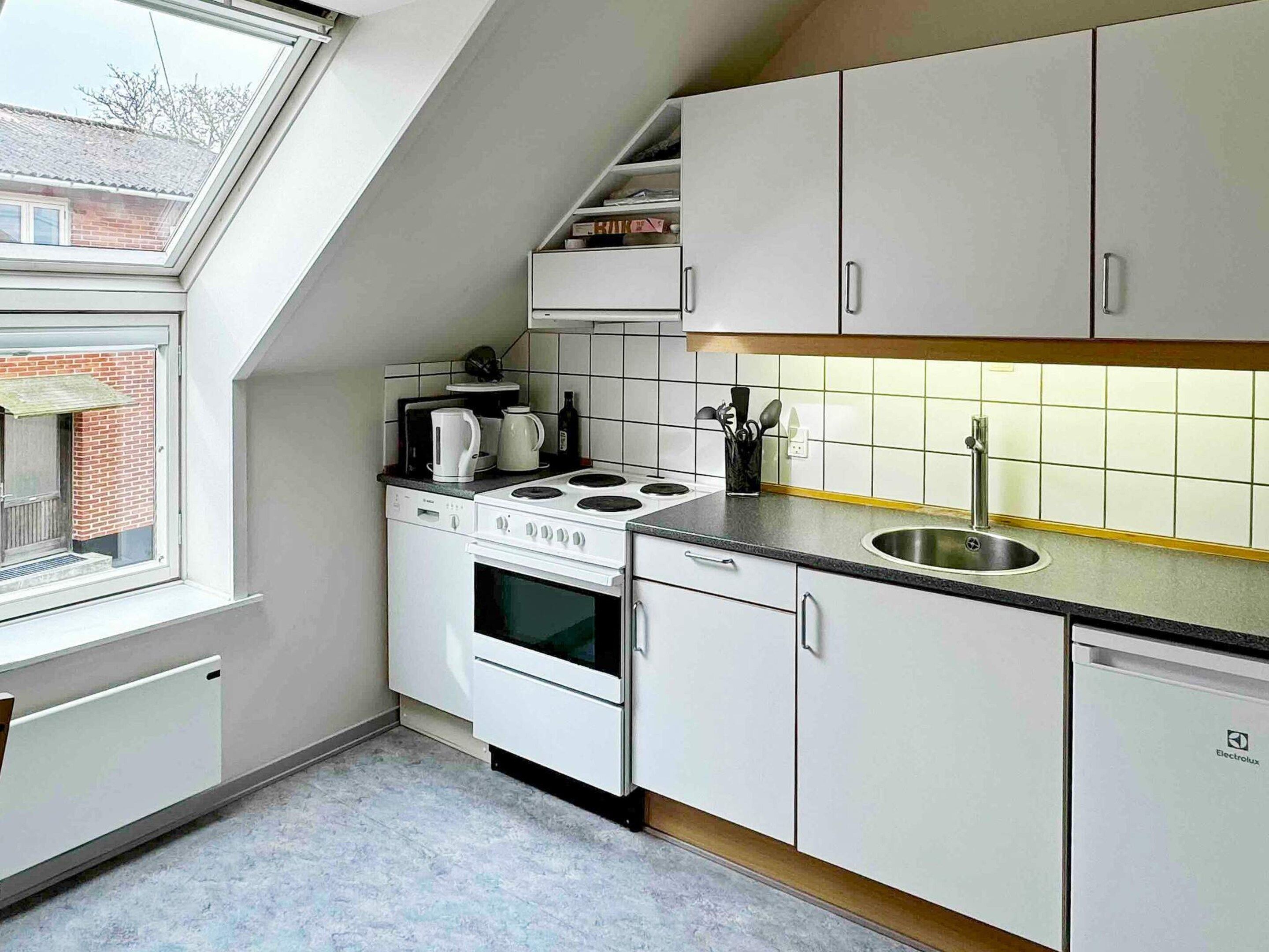 Une cuisine de taille réduite avec des meubles blancs, une cuisinière, un four et un évier.