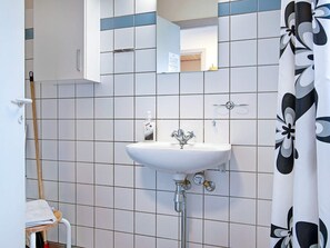 A bathroom with a white sink, a mirror, and a shower curtain with a floral pattern. - 4 Person Holiday Home in Gudhjem (Gudhjem)