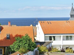 A coastal residential area with terracotta-tiled roofs, a white building with a balcony, and a clear view of the sea. - 4 Person Holiday Home in Gudhjem (Gudhjem)