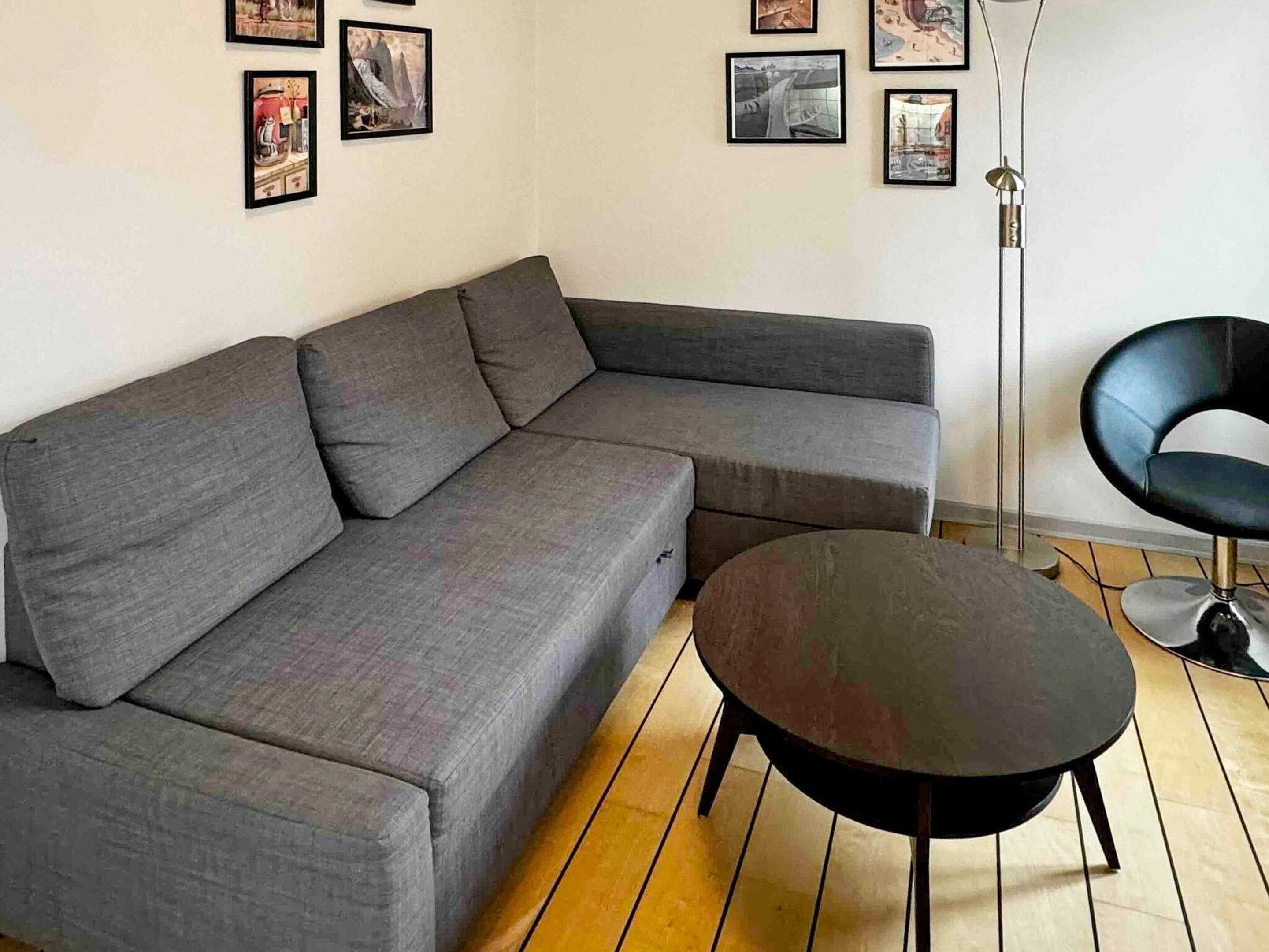 Un salon moderne avec un canapé d’angle gris, une table basse ronde noire et un fauteuil noir.