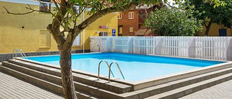 A swimming pool with steps leading into it, surrounded by a white fence and a tree.