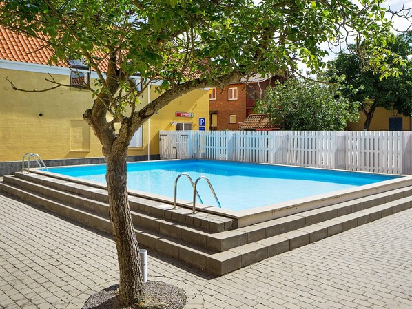 A swimming pool with steps leading into it, surrounded by a white fence and a tree. - 4 Person Holiday Home in Gudhjem (Gudhjem)