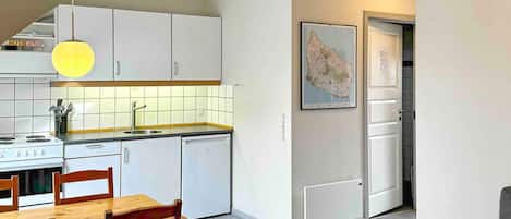 A modern kitchen with white cabinets, a wooden dining table, and a map on the wall.