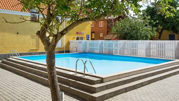A swimming pool with steps leading into it, surrounded by a white fence, and a tree in the foreground.