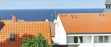 Ein Küstenwohngebiet mit terrakottafarbenen Dächern, einem weißen Gebäude mit Balkon und freiem Blick auf das Meer.