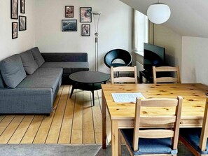 Una sala de estar moderna con sofá, una mesa redonda y sillas, una mesa de comedor con papeles y una obra de arte en la pared.