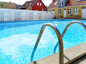 Una piscina con barandillas de metal, rodeada por una valla blanca y casas con fachadas rojas y amarillas.