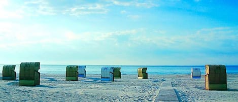 A beach with a wooden boardwalk leading to beach huts numbered 97, 99, and 64.