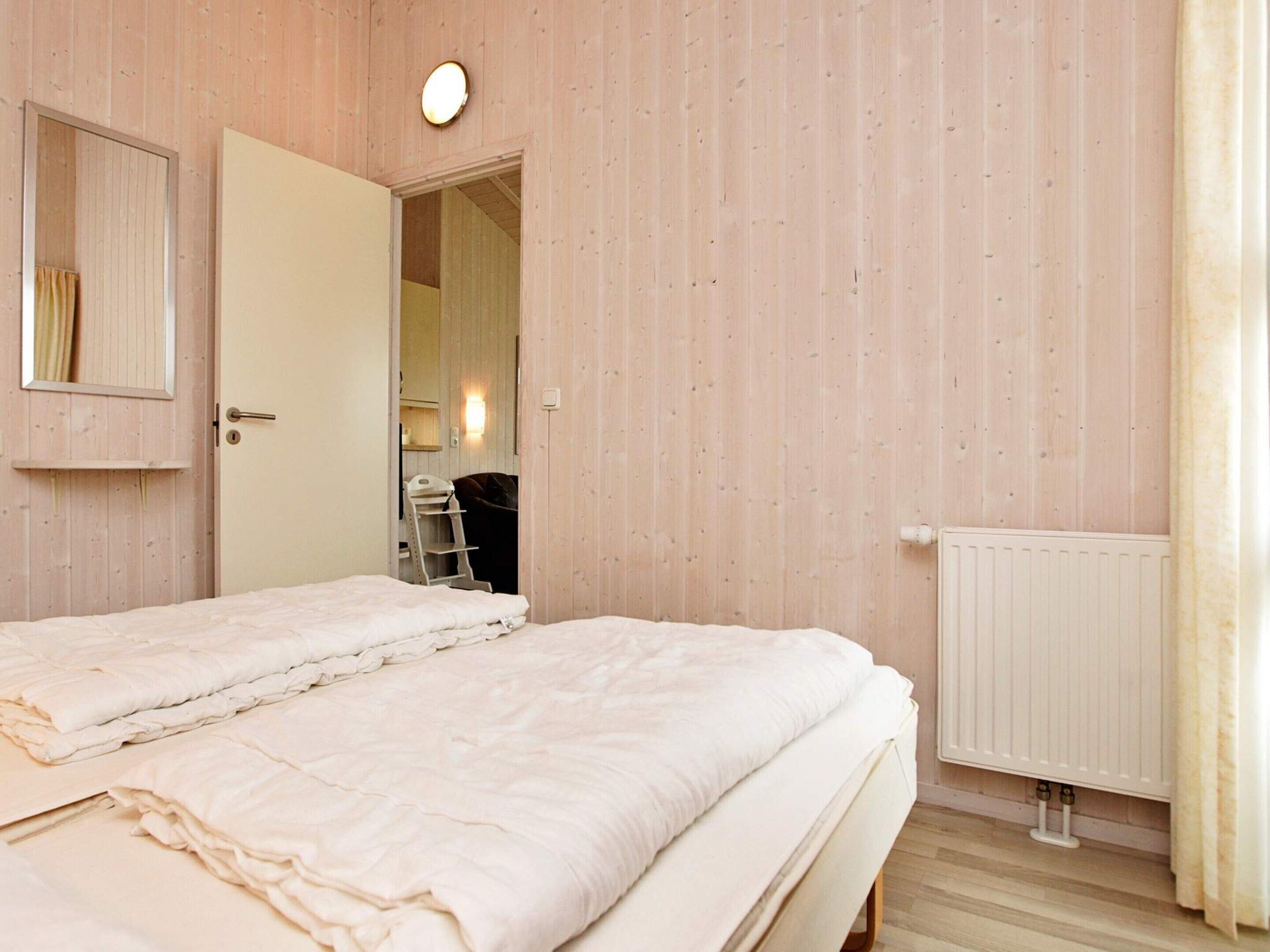 Une chambre avec deux lits, une porte donnant sur une salle de bain, un radiateur et un miroir au mur.