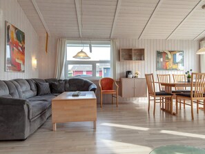 A modern living room with a sofa, coffee table, and dining area with chairs and a cabinet.