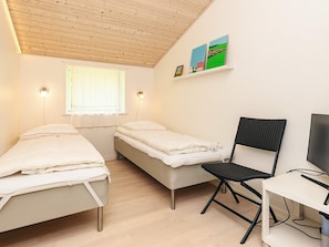 A dormitory room with two single beds, a desk with a chair, a TV, and a window with curtains.