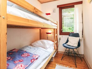 A bunk bed room with a desk and chair, a window with curtains, and a wall-mounted light.