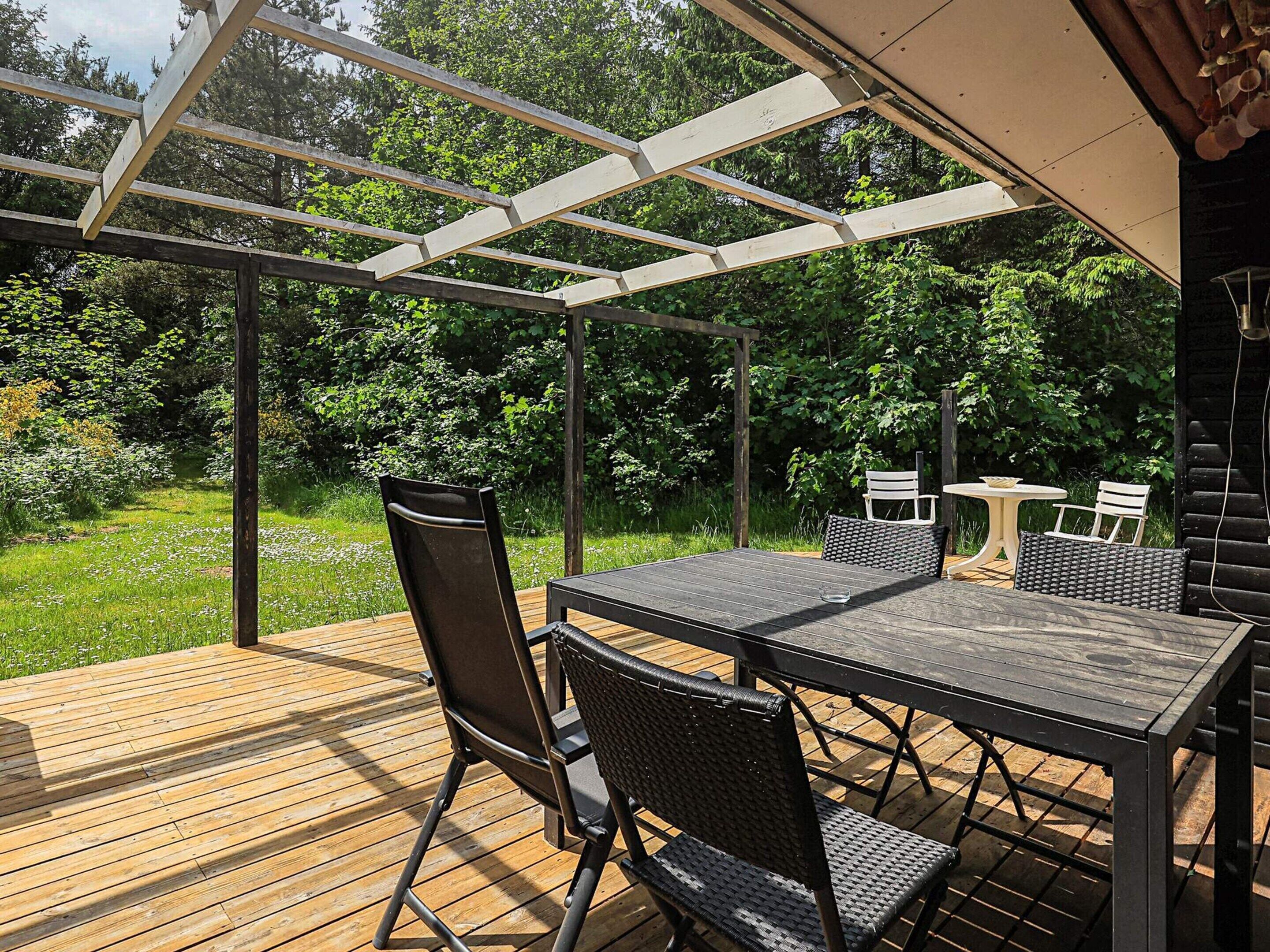 An outdoor patio with a wooden deck, a pergola, and a table with chairs.