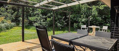 Un patio exterior con terraza de madera, un pérgola y una mesa con sillas.