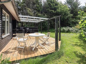 A wooden deck with a round table and chairs, a grill, and a pergola structure.