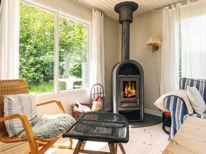 A cozy room with a wood-burning stove, wicker furniture, and a view of greenery outside.
