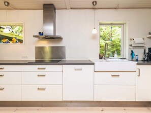 A modern kitchen with white cabinets, a stainless steel range hood, a double sink, and a window with a view of greenery.