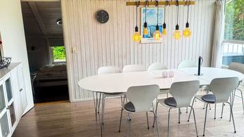A modern dining area with a white table and chairs, a clock on the wall, and hanging light bulbs.