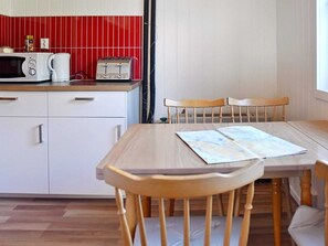 Uma cozinha compacta com micro-ondas, torradeira e cafeteira na bancada, uma mesa de jantar com cadeiras, e um revestimento de azulejos vermelhos.