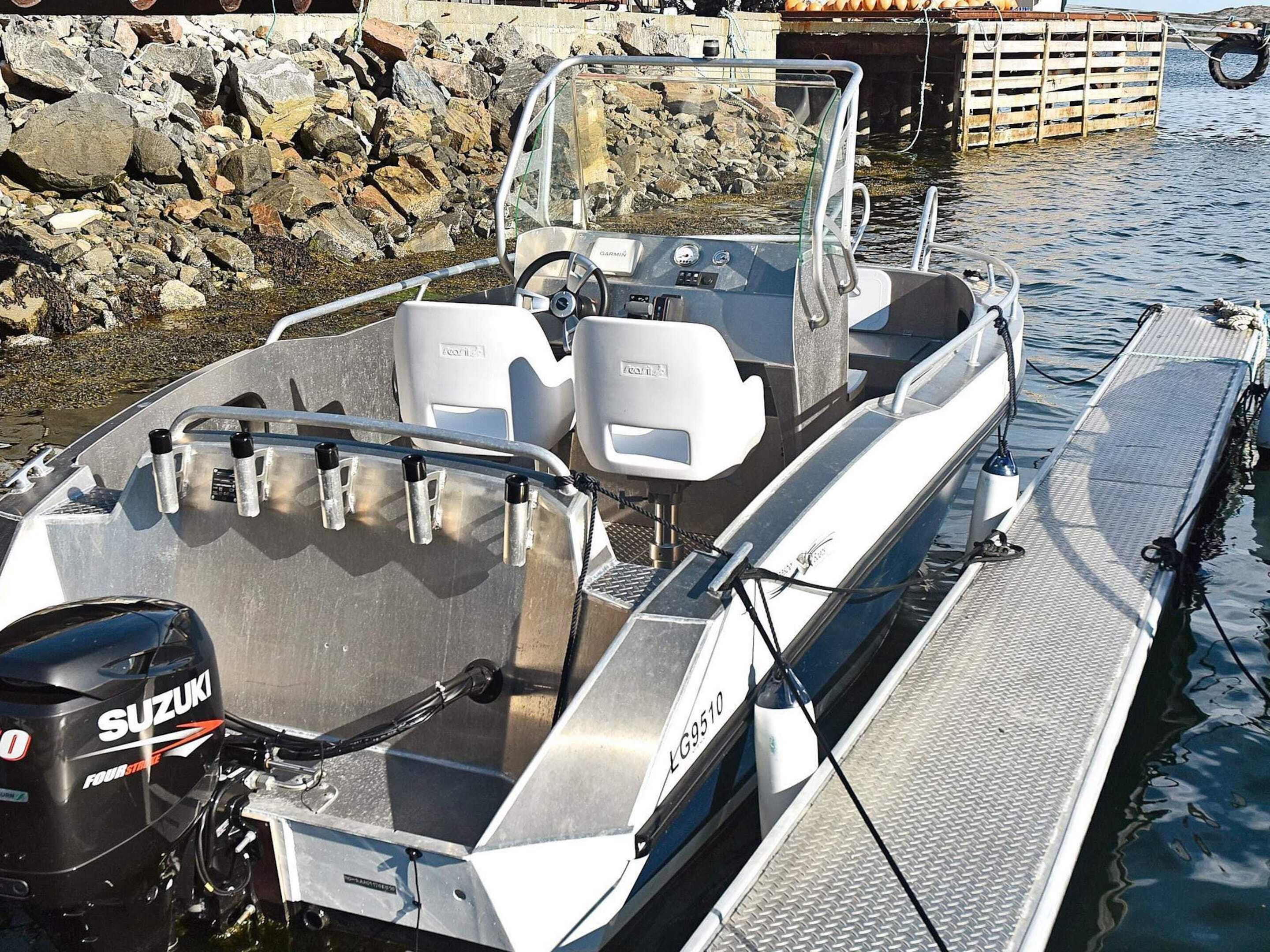 A motorboat docked at a pier with a rocky shoreline in the background.