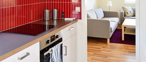 A compact kitchen with a red backsplash, a built-in oven, and a dining area with a sofa and table.