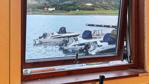 A window view of a dock with boats, a mountain in the background, and a red building. - 8 Person Holiday Home in Oksvoll (Orland)