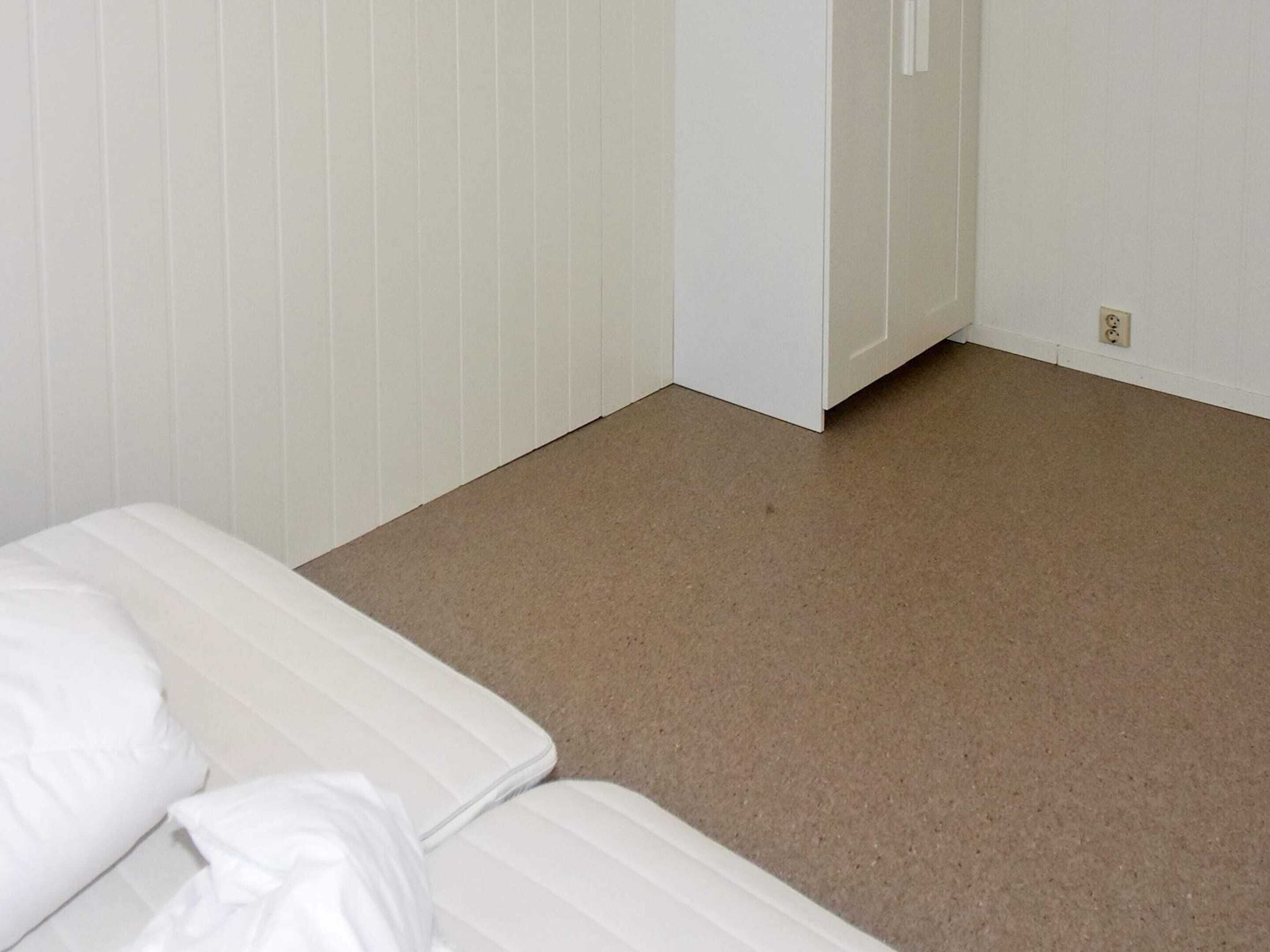 Une chambre avec un lit blanc et un tapis marron.