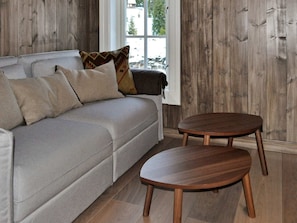 A room with a grey sofa, two round wooden tables, and a window with a view of trees.