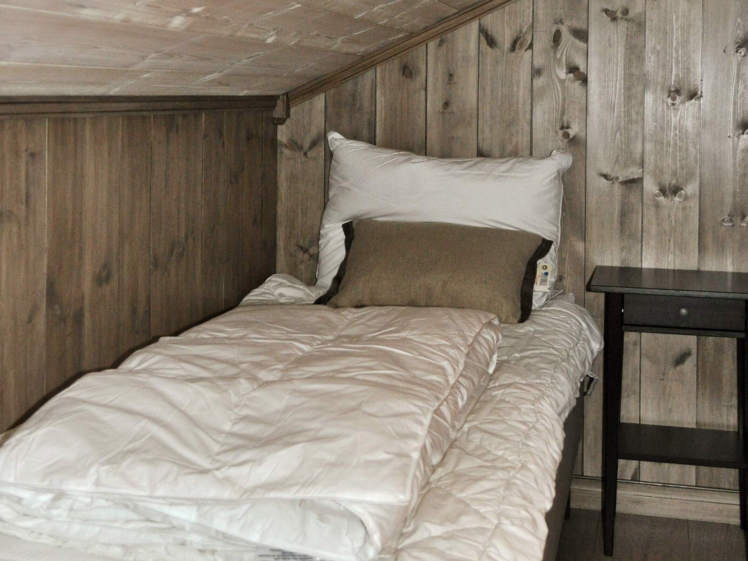 A single bed with a white and beige duvet, a wooden headboard, and a small bedside table.