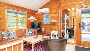 A cozy cabin interior with a wooden interior, a television, a dining area, and a seating area with cushions. - 4 Person Holiday Home in Bindslev (Bindslev)