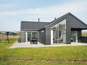 A modern house with a large glass door, a patio with a table and chairs, and a grassy yard. - Enchanting Holiday Home in Jutland by the Sea (Haderslev)