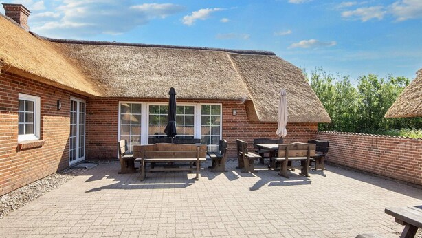 A brick building with a thatched roof, outdoor seating area with wooden tables and benches, and a paved patio. - Cozy Holiday Home in Ulfborg near Sea (Ulfborg)