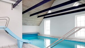 An indoor swimming pool with a blue slide, tiled floor, and a glass table in the foreground. - Cozy Holiday Home in Ulfborg near Sea (Ulfborg)