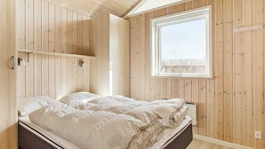 A bedroom with a bed, wooden walls, a window, and a shelf.