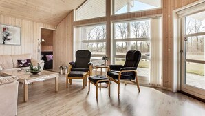 A spacious room with wooden floors, a large window, and a cozy seating area with a sofa and two armchairs.