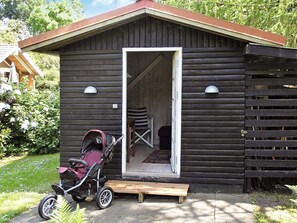 A wooden cabin with a door open, revealing a staircase inside, a stroller parked outside, and a small wooden bench. - Vibrant Holiday Home in Nykobing Sj near Sea (Nykobing Sjaelland)
