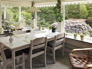 A dining area with a table set for four, surrounded by chairs, with a view of greenery and flowers through large windows. - Vibrant Holiday Home in Nykobing Sj near Sea (Nykobing Sjaelland)