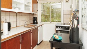 A kitchen with wooden cabinets, a black countertop, a stove, and a window with a view of greenery. - Vibrant Holiday Home in Nykobing Sj near Sea (Nykobing Sjaelland)