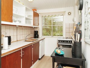 Cocina con armarios de madera, encimera negra, estufa y ventana con vistas a la vegetación.