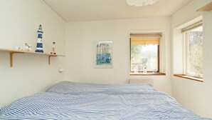 A bedroom with a bed, a window, a lamp, and a shelf with decorative items. - Vibrant Holiday Home in Nykobing Sj near Sea (Nykobing Sjaelland)