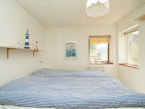 Un dormitorio con cama, ventana, lámpara y estante con adornos.