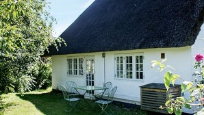 Uma casa de campo branca com telhado de palha, um pequeno jardim e uma mesa com cadeiras.