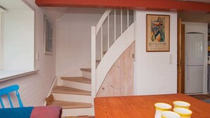 Um quarto com uma escada de madeira, uma mesa de jantar com chávenas amarelas e um cartaz na parede.