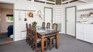 Un coin repas avec une table et des chaises en bois, un luminaire suspendu et une vue sur la cuisine.