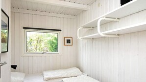 Une petite cabane d’une seule pièce, avec deux lits, une fenêtre donnant sur la verdure et un lit superposé sur le côté droit.