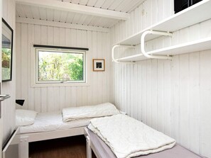 A small, single-room cabin with two beds, a window with a view of greenery, and a bunk bed on the right.