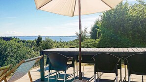 Une terrasse extérieure avec une table et des chaises, un grand parasol et une vue sur la mer.