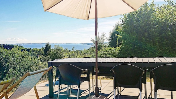 Une terrasse extérieure avec une table et des chaises, un grand parasol et une vue sur la mer.